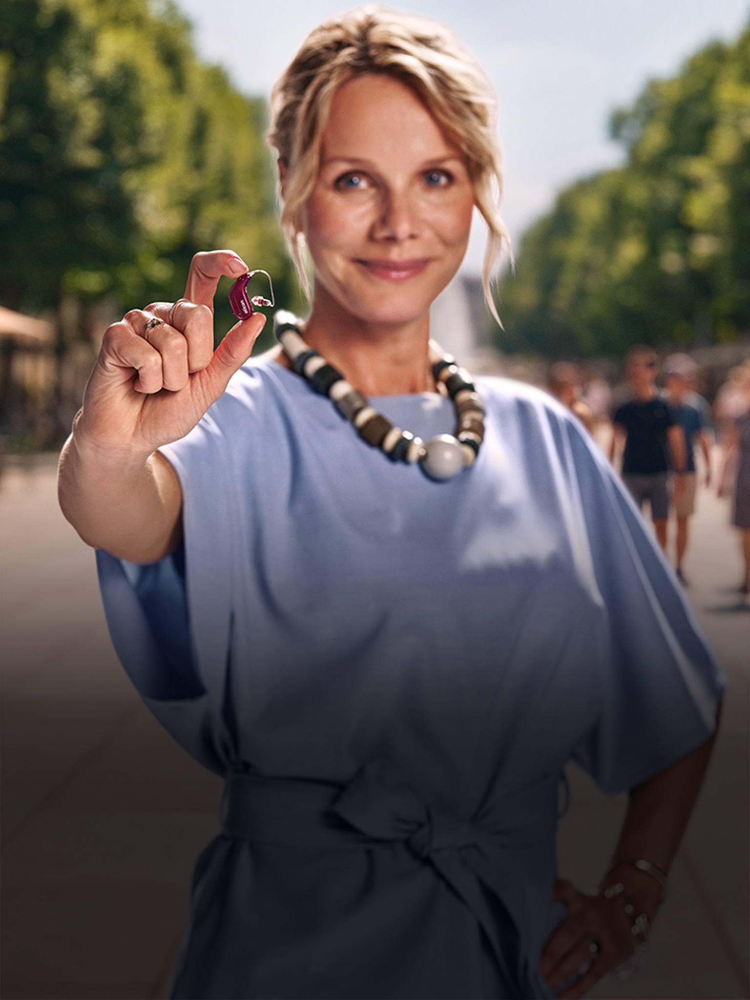 Woman holding an Oticon Reveal hearing aid outdoors