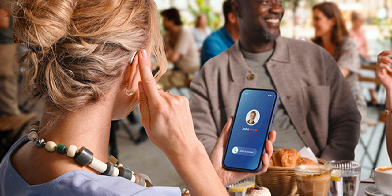 Frau im Café tippt an ihr Ohr und nimmt über das Smartphone ein Telefonat an
